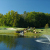 A view of a green with water fountain in foreground at Hideaway Lake Club.